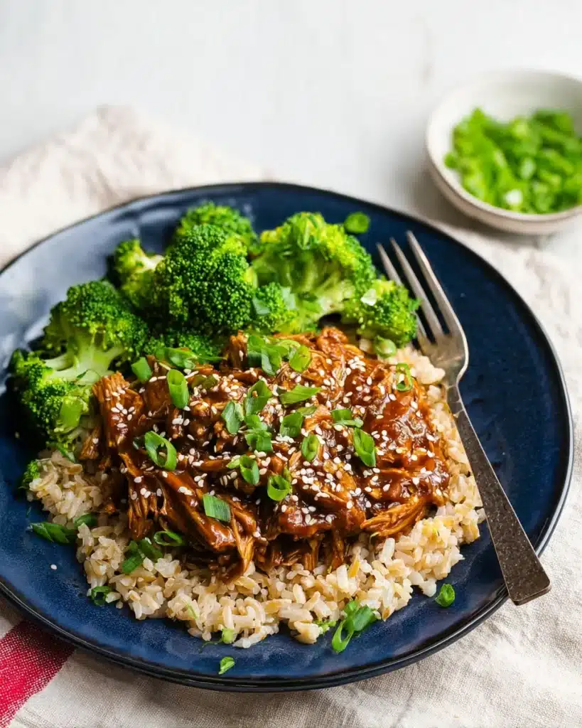 Slow cooker honey garlic chicken with brown rice and broccoli, topped with sesame seeds and green onions.