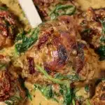 Close-up of creamy Slow Cooker Tuscan Chicken thighs with sun-dried tomatoes and spinach in a rich herb cream sauce