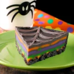 Spiderweb Brownie Tart slice with colorful Halloween layers on green plate with spider-decorated milk glass.