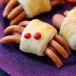 Close-up of spooky spider hot dogs wrapped in golden crescent dough with ketchup eyes on a festive plate.