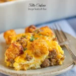 A slice of Tater Tot Sausage Breakfast Casserole with crispy tots, melted cheese, and sausage on a white plate.