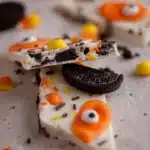 White chocolate Halloween Oreo bark topped with Oreos, candy eyeballs, and festive sprinkles on a rustic surface.