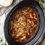 Crock pot bourbon chicken in glossy sauce with green onions and rice