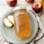 Homemade Apple Juice Recipe : Easy Canning Instructions 14 Homemade apple juice in a mason jar with red apples and a rustic background