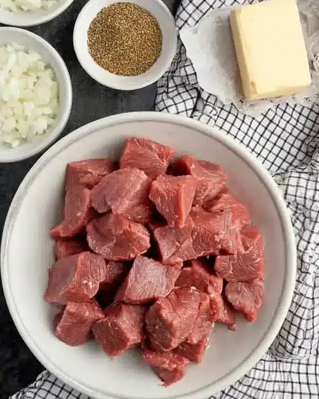 Overhead shot of raw ingredients for crockpot steak bites including beef cubes, garlic, onions, and butter

