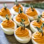 Thanksgiving Deviled Eggs – A Festive Holiday Appetizer 14 Thanksgiving deviled eggs with orange filling and fresh herbs on rustic platter