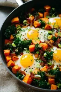 Sweet potato breakfast hash with eggs, kale, and crispy bacon in skillet