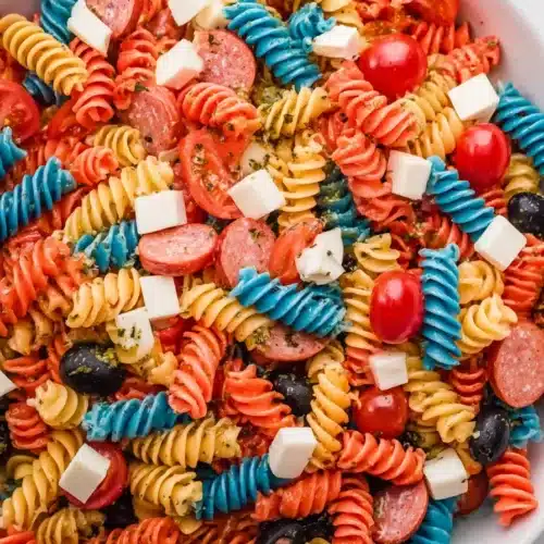 Red white and blue pasta salad with tomatoes, mozzarella, olives, and pepperoni in a bowl