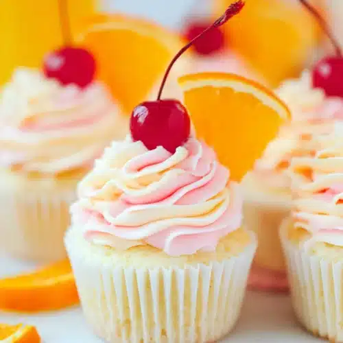 Tequila Sunrise Cupcakes (Bright & Boozy Cinco de Mayo Dessert) 3 Tequila Sunrise Cupcakes with pink swirl frosting cherries and orange slices