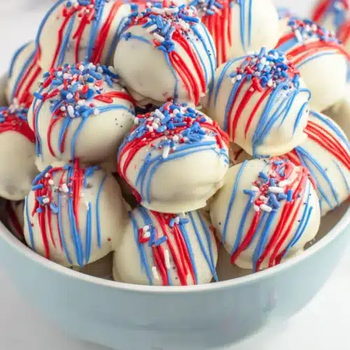Patriotic Oreo Balls with white chocolate, red and blue drizzle, and festive sprinkles
