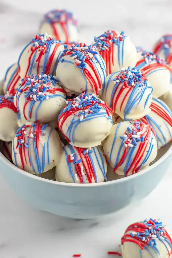 Patriotic Oreo Balls with white chocolate, red and blue drizzle, and festive sprinkles