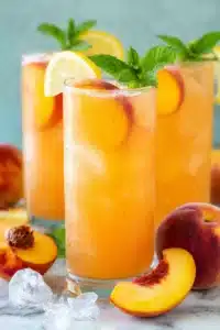 Fresh peach lemonade with lemon slices, mint, and ice in tall glasses