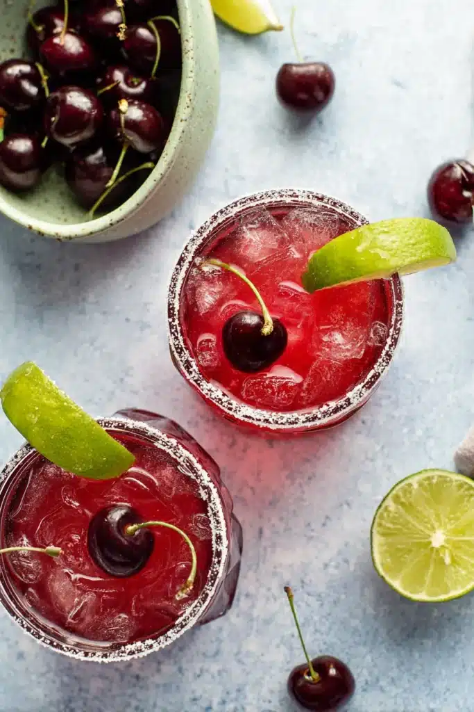 Top view of Spiked Cherry Limeade cocktails with cherries, lime wedges, and sugared rims