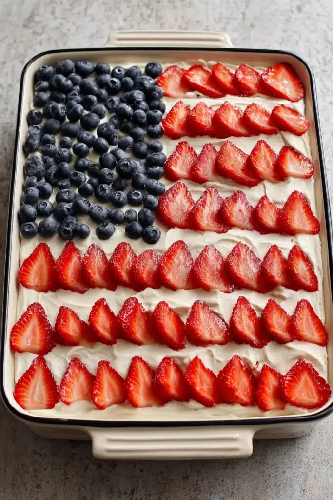 American Flag Strawberry Poke Cake decorated with strawberries and blueberries