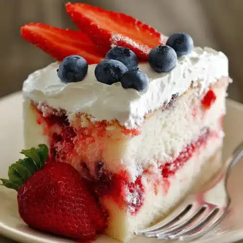 American Flag Strawberry Poke Cake slice with cream cheese frosting and fresh berries