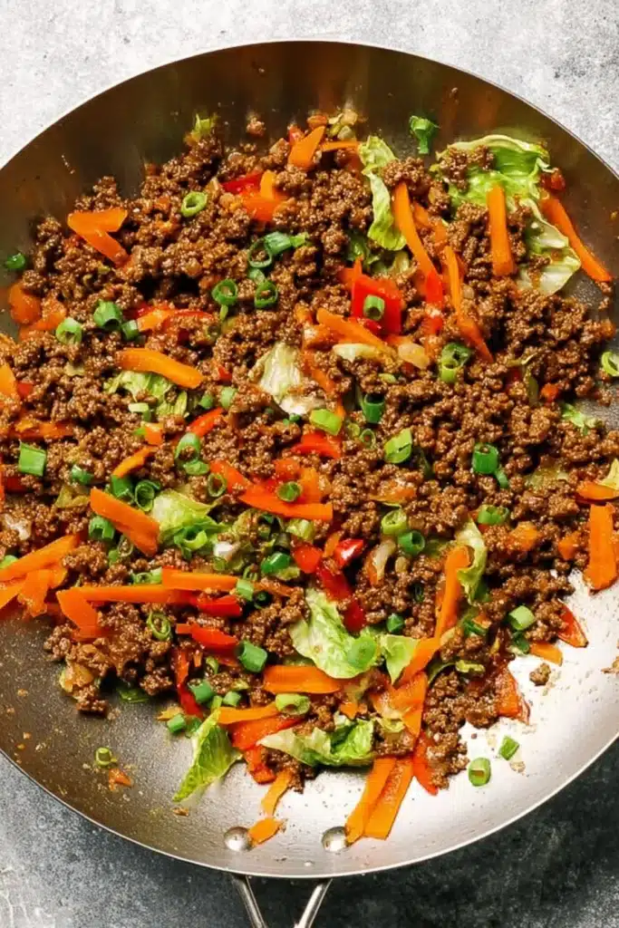 Ground Beef Lettuce Wraps filling cooking in a skillet with peppers, carrots, and green onions