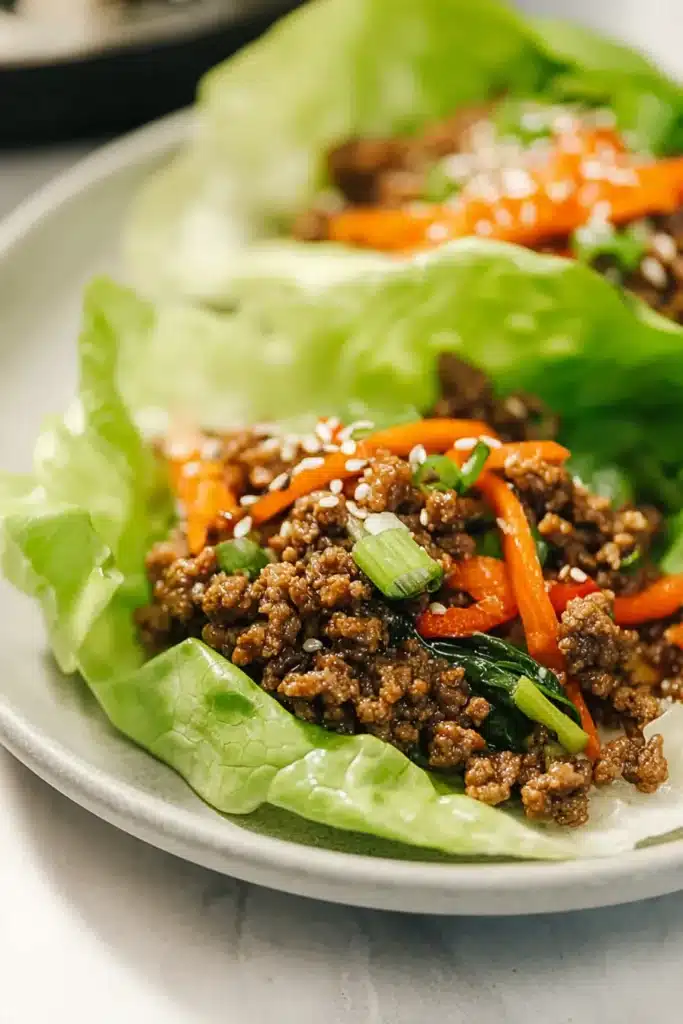 Ground Beef Lettuce Wraps with sesame seeds, carrots, and peppers in crisp butter lettuce cups